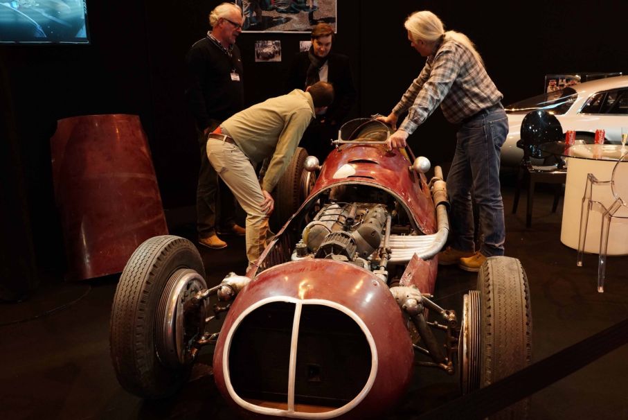 En Maserati monoposto ännu dammig från sin senaste insats manövreras in i montern.